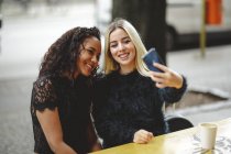 Schöne junge Frauen sitzen in Berliner Straßencafé und machen Selfie — Stockfoto