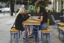 Вид сбоку красивых молодых женщин, сидящих в берлинском уличном кафе, говорящих и смеющихся — стоковое фото