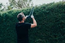 Hombre caucásico recortando un seto arizonica con tijera grande para jardín - foto de stock