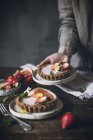 Unrecognizable person serving plates of garnished citrus cakes with strawberries on wooden table — Stock Photo
