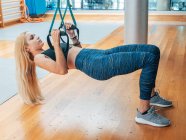 Young woman in sportswear holding on trx bands doing workout in gym — Stock Photo