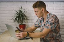 Концентрированный человек с помощью смартфона во время использования ноутбука за столом в кафе — стоковое фото