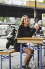 Beautiful cheerful woman drinking coffee in Berlin street cafe on blurred urban background — Stock Photo