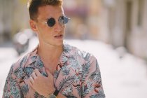 Schöner Mann in hawaiianischem Hemd, der mit Sonnenbrille auf der Straße steht und wegschaut — Stockfoto