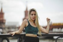 Modelo feminino loira bonita inclinado em grade no dia de verão em Berlim no fundo borrado olhando para a câmera — Fotografia de Stock