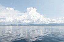 Живописный вид на облачное небо и голубую воду с отдаленной лодкой в лучах солнца, Халкидики, Греция — стоковое фото