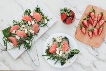 Top view of bowls with strawberries, grapefruit and rocket salad on table served on boards — Stock Photo