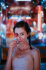Mulher com cabelo trançado pigtail segurando pirulito no parque de diversões na noite quente de verão no fundo borrado — Fotografia de Stock