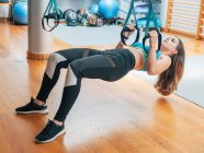 Mujer joven en ropa deportiva sosteniendo bandas trx haciendo ejercicio en el gimnasio - foto de stock