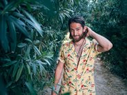 Pensive handsome bearded hipster man walking in jungle looking in camera — Stock Photo