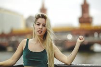 Блондинка-модель прислонилась к перилам в летний день в Берлине на размытом фоне, глядя в камеру — стоковое фото