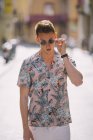 Bonito macho em camisa havaiana de pé na rua com óculos de sol — Fotografia de Stock