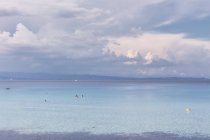 Миролюбивая морская вода с людьми, купающимися в спокойной погоде под облачным небом, Халкидики, Греция — стоковое фото