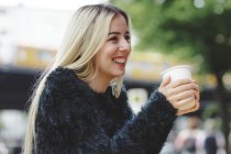 Hermosa mujer alegre bebiendo café en el café de la calle de Berlín sobre fondo urbano borroso. - foto de stock