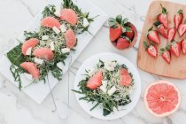 Top view of bowls with strawberries, grapefruit and rocket salad on table served on kitchen boards — Stock Photo