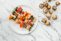 Pieces of cherry tomatoes, sweet peppers, salmon and mushrooms served on skewers on table with mushrooms — Stock Photo