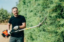 Кавказский человек обрезает изгородь из оризоники механическими инструментами — стоковое фото