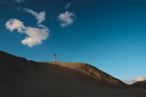 Donna in abito bianco in piedi in lontananza sulla collina di sabbia illuminata dal sole a Tarifa, Spagna con cielo blu e nuvola bianca — Foto stock