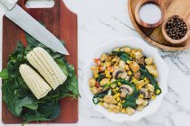 Served bowl with mushrooms, corn and cut chicken on table with corn leaves of greenery on cutting board and condiments — Stock Photo