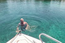 De cima homem idoso com natação em água limpa fresca perto de iate no dia de verão, Halkidiki, Grécia — Fotografia de Stock