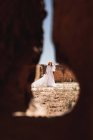 Through hole view of elegant woman in white dress inside walls of ancient fortress on daytime — Stock Photo