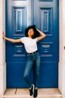 Pretty ethnic woman in white t-shirt and jeans leaning on blue door with closed eyes — Stock Photo