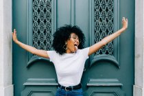 Young African American woman standing with closed eyes by green wooden door and sticking out tongue — Stock Photo
