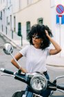Молодая афроамериканка с черными вьющимися волосами сидит на мотоцикле и смотрит в сторону солнцезащитных очков — стоковое фото