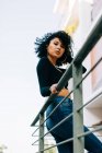 Чуттєва молода жінка з Кучеряве волосся стоячи на балконі, спираючись на перила і дивлячись на камеру — стокове фото