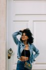 Trendy African American woman in black crop top and jeans standing by door — Stock Photo