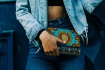 African american woman in jeans and denim jacket standing with trendy colorful clutch in hand — Stock Photo
