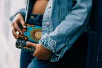 Africano mulher americana em jeans e jaqueta jeans de pé com embreagem colorida na moda na mão — Fotografia de Stock