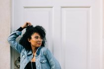 Привычная афроамериканка в черном топе и джинсах стоит у двери и смотрит в камеру — стоковое фото