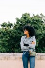 Young trendy African American woman in jeans and crop top sitting on stone parapet — Stock Photo