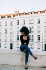 Giovane donna afroamericana di tendenza in jeans e crop top seduta su parapetto in pietra — Foto stock