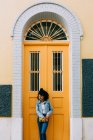 Young African American woman in jeans and denim jacket leaning on yellow door, holding clutch and looking away — Stock Photo
