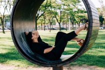 Vista laterale della donna sdraiata su una panchina creativa a forma di anello e sorridente a Lisbona durante l'estate — Foto stock