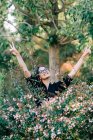 Hermosa mujer morena en gafas de pie entre arbustos florecientes en el parque y mirando hacia otro lado en Lisboa - foto de stock