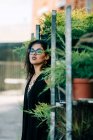 Trendige Frau in Spitzenoberteil lehnt an Gestellen mit Topfpflanzen und blickt in Lissabon in die Kamera — Stockfoto