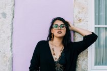 Приваблива молода жінка в окулярах і чорна блузка стоїть біля барвистого вінтажного муру і дивиться на камеру в Лісабоні. — стокове фото