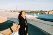 Mulher bonita e elegante em roupa preta em pé pela ponte com a paisagem da cidade em Lisboa no dia ensolarado — Fotografia de Stock