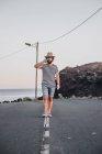 Homme barbu en chapeau marchant sur une route déserte et parlant au téléphone — Photo de stock
