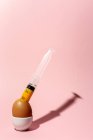 Cooking egg in eggcup with syringe taking out yellow raw yolk on pink background — Stock Photo
