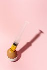 Cuisson des œufs dans une coquille d'oeuf avec seringue sortant jaune jaune jaune brut sur fond rose — Photo de stock