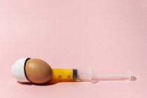 Uovo di cottura in eggcup con siringa tirando fuori giallo tuorlo crudo su sfondo rosa — Foto stock