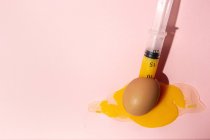 Cooking egg in eggcup with syringe taking out yellow raw yolk on pink background — Stock Photo
