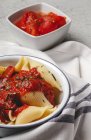 Deliciosa pasta conchiglie espolvoreada con albahaca y salsa de tomate rojo servido en plato blanco - foto de stock