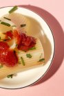 Gekochte Cannelloni mit Tomatensauce und Kräutern auf weißem Teller vor rosa Hintergrund — Stockfoto