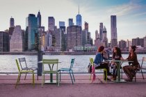 Друзья сидят на террасе с нью-йоркским фоном вечером — стоковое фото
