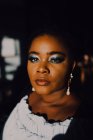 Portrait de belle jeune femme noire incurvée avec un maquillage lumineux en robe hors épaule regardant la caméra — Photo de stock